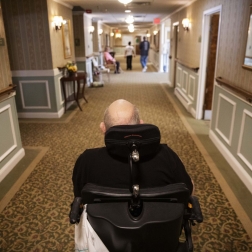 elderly man in wheelchair going down a corridor